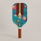 Front view face of RallyStand luxury designer pickleball paddle featuring a teal monogram pattern, red and green stripes, golden zipper graphic, and vibrant floral embroidery details.