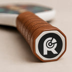 Close-up of the RallyStand luxury pickleball paddle handle showing the premium brown stitched leather grip and the custom "R" logo printed on the butt cap.